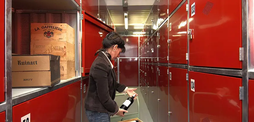 Une personne tient une bouteille de vin à côté de boxes de stockage